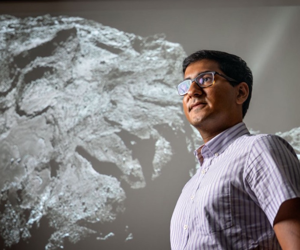 Doctoral student Abhinav Jindal, standing in front of a Rosetta mission image of Comet 67P, modeled the evolution of smooth terrain on that frozen world.